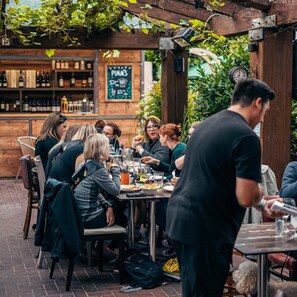 A group of people dining outdoors at a restaurant with a wooden pergola and a brick floor.