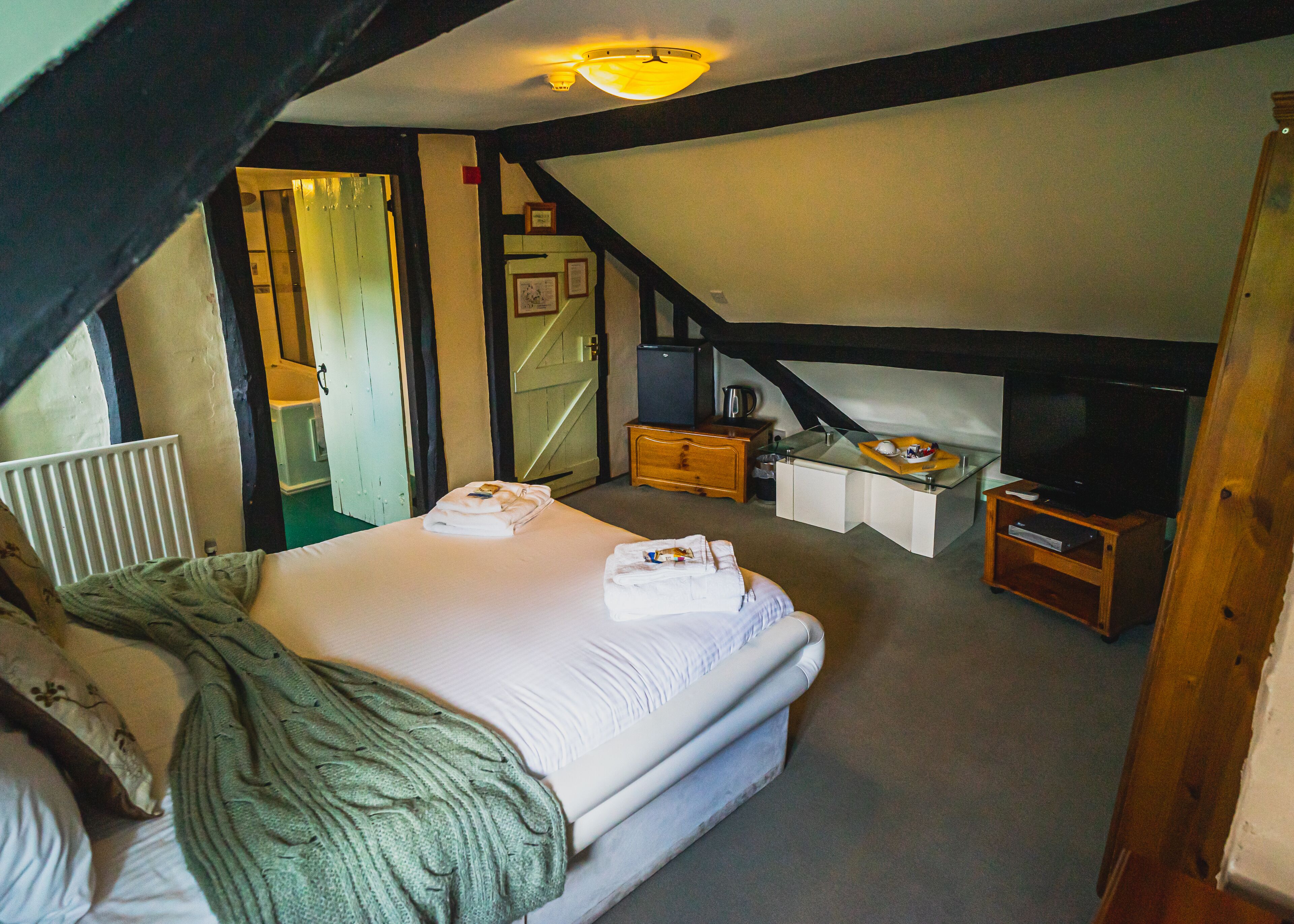A bedroom with a bed, a television, a small wooden cabinet, and a radiator.