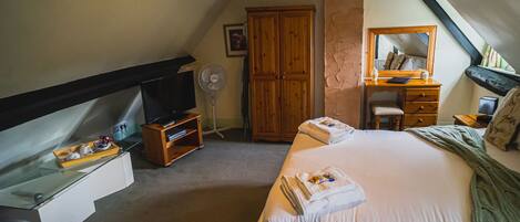 A bedroom with a bed, a wooden dresser, a television, and a desk with a chair.