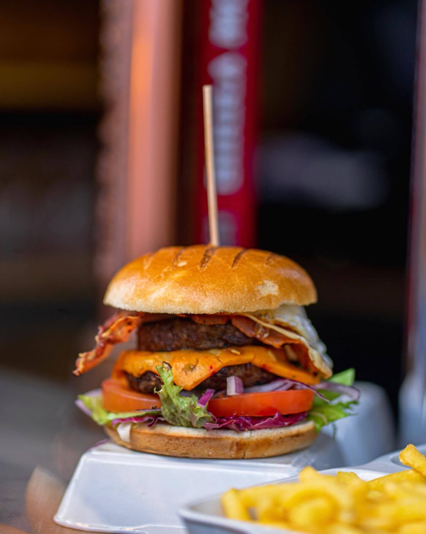 Una hamburguesa con pan tostado, lechuga, tomate y una porción de papas fritas.
