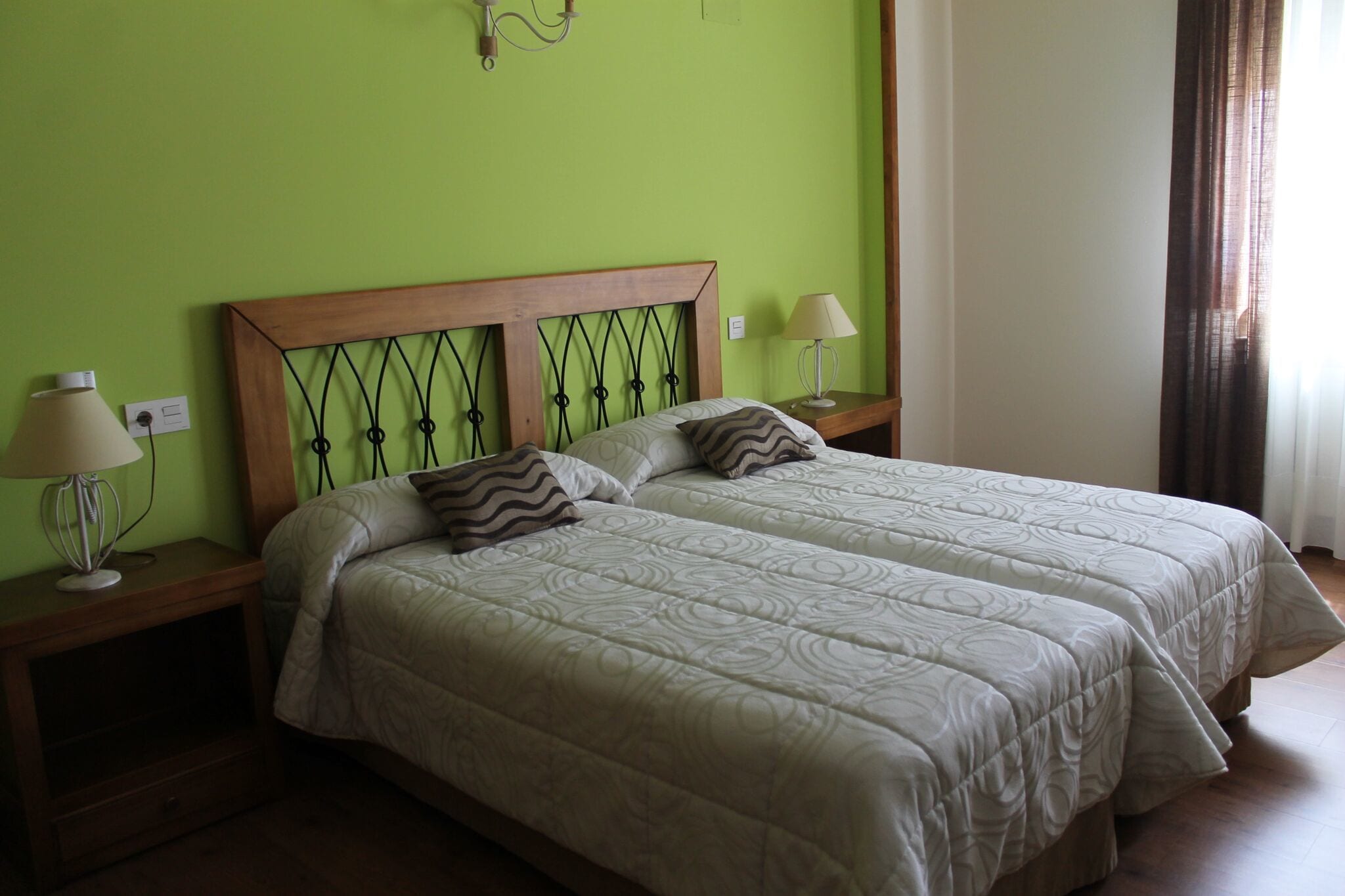 Una cama doble con cabecera de madera y dos mesitas de noche, cada una con una lámpara.