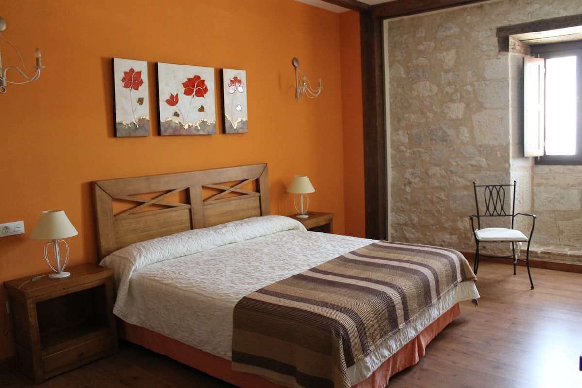 Une chambre à coucher avec un lit en bois, deux tables de chevet avec des lampes, une chaise et des œuvres d’art accrochées au mur.