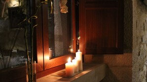 Una habitación tenuemente iluminada con una pared de piedra, un armario de madera y una estantería de cristal con velas.