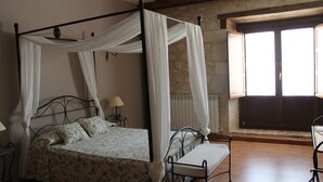Una cama con dosel y cuatro columnas, una mesita de noche con lámpara, y un banco.