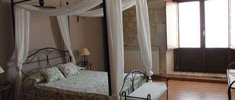 A four-poster bed with a canopy, a bedside table with a lamp, and a bench.
