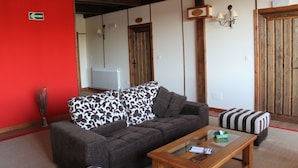 Una habitación con una pared roja, un sofá con cojines estampados, un reposapiés a rayas y una mesa de centro de madera.