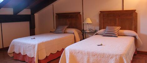 Two single beds with wooden headboards and red skirts, a nightstand with a lamp, and a sloped ceiling with exposed beams.