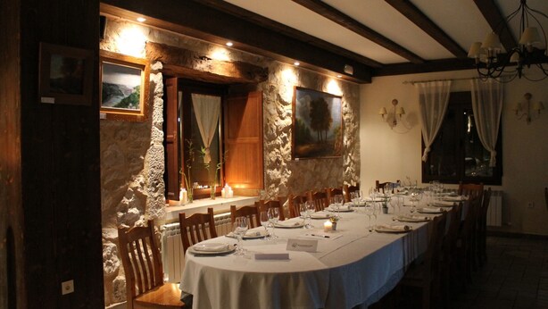 Una larga mesa de comedor preparada para una comida en una habitación con paredes de piedra y vigas de madera.