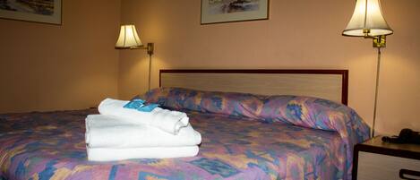 Una habitación de hotel con una cama, dos lámparas adosadas a la pared y dos cuadros enmarcados.