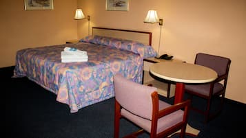 Una habitación de hotel con una cama, dos sillas, una mesita y dos lámparas de pared.