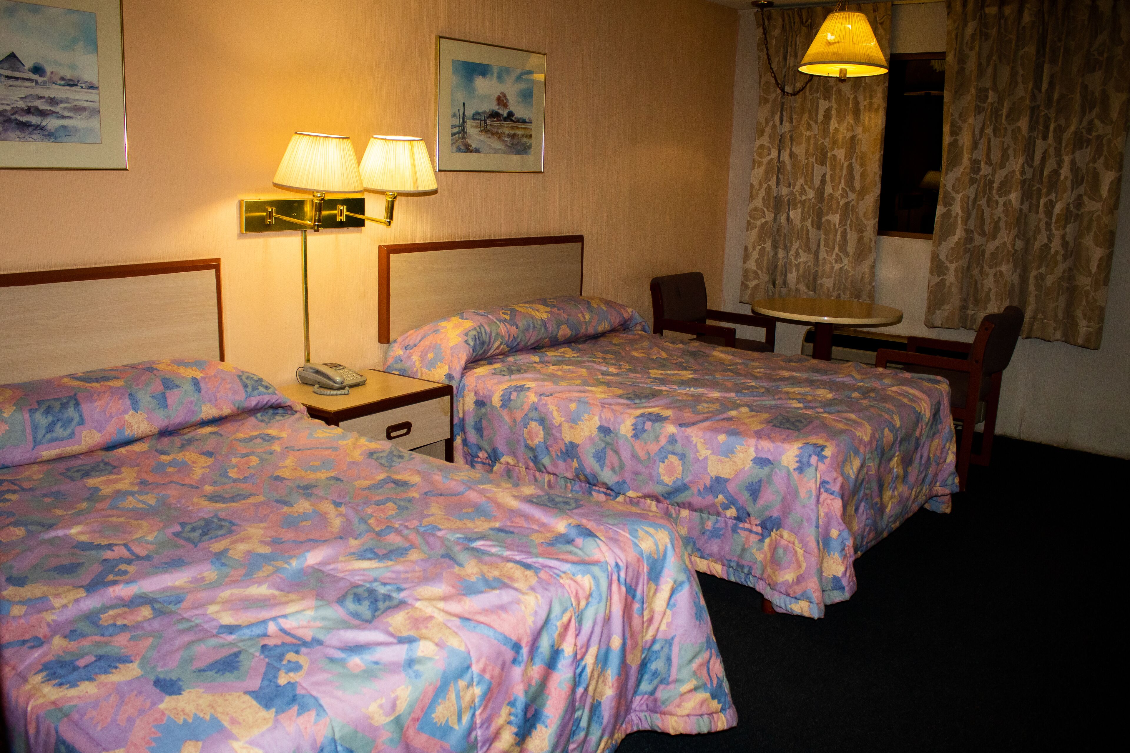 A hotel room with two beds, a small table, a chair, and a lamp.