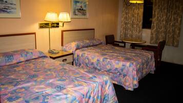 A hotel room with two beds, a small table, a chair, and a lamp.