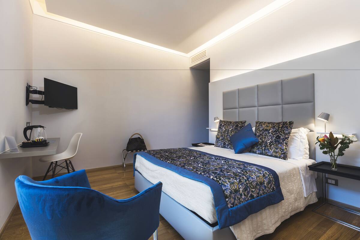 Une chambre d’hôtel moderne équipée d’un lit, d’un bureau, d’une chaise, d’une télévision et d’une table de chevet avec une lampe.