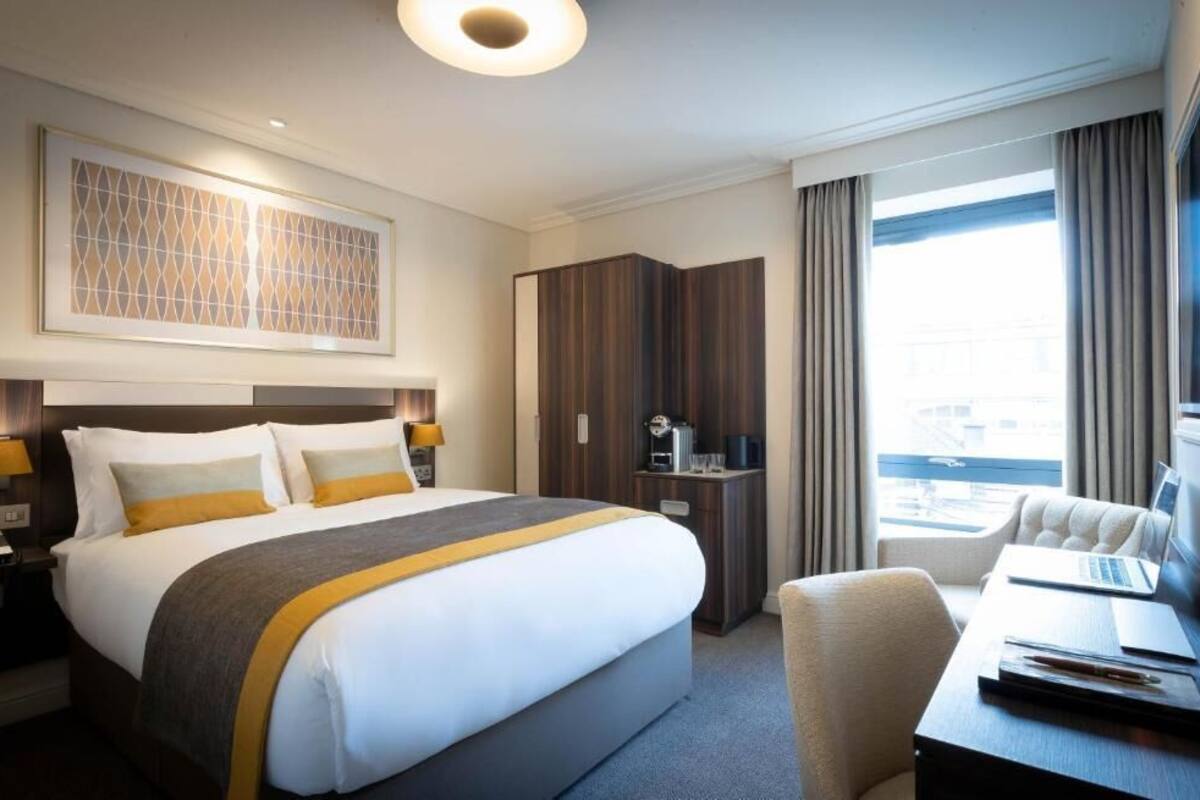 Habitación de hotel con una cama grande, un escritorio con una computadora portátil, un armario y vistas a la ciudad.