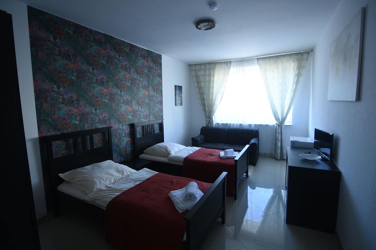 A hotel room with two beds, a desk, a TV, and a window with curtains.