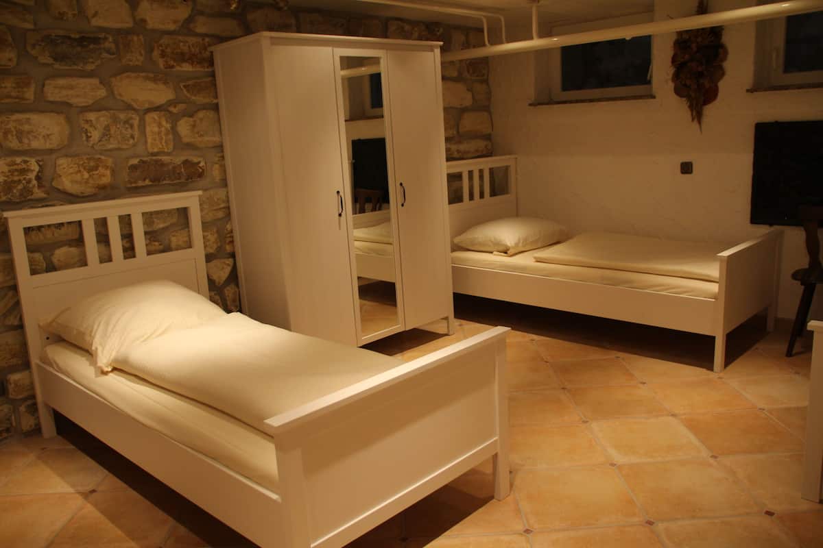 A bedroom with two single beds, a wardrobe, and a stone wall.