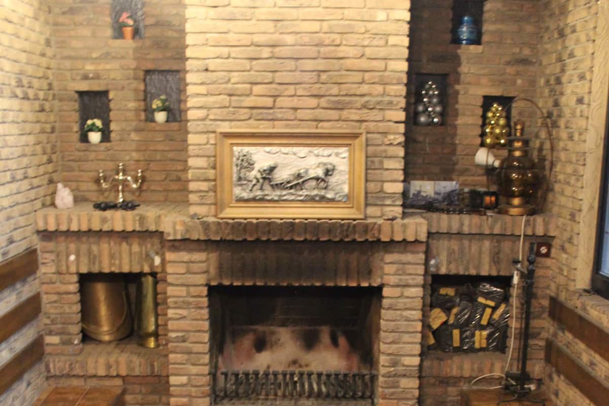A room with a brick fireplace, a large ornate rug, and a framed picture above the mantel.