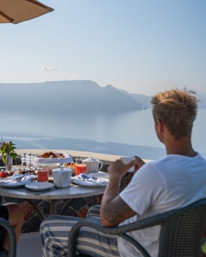 Eine Person sitzt an einem Tisch im Freien mit Blick auf das Meer.