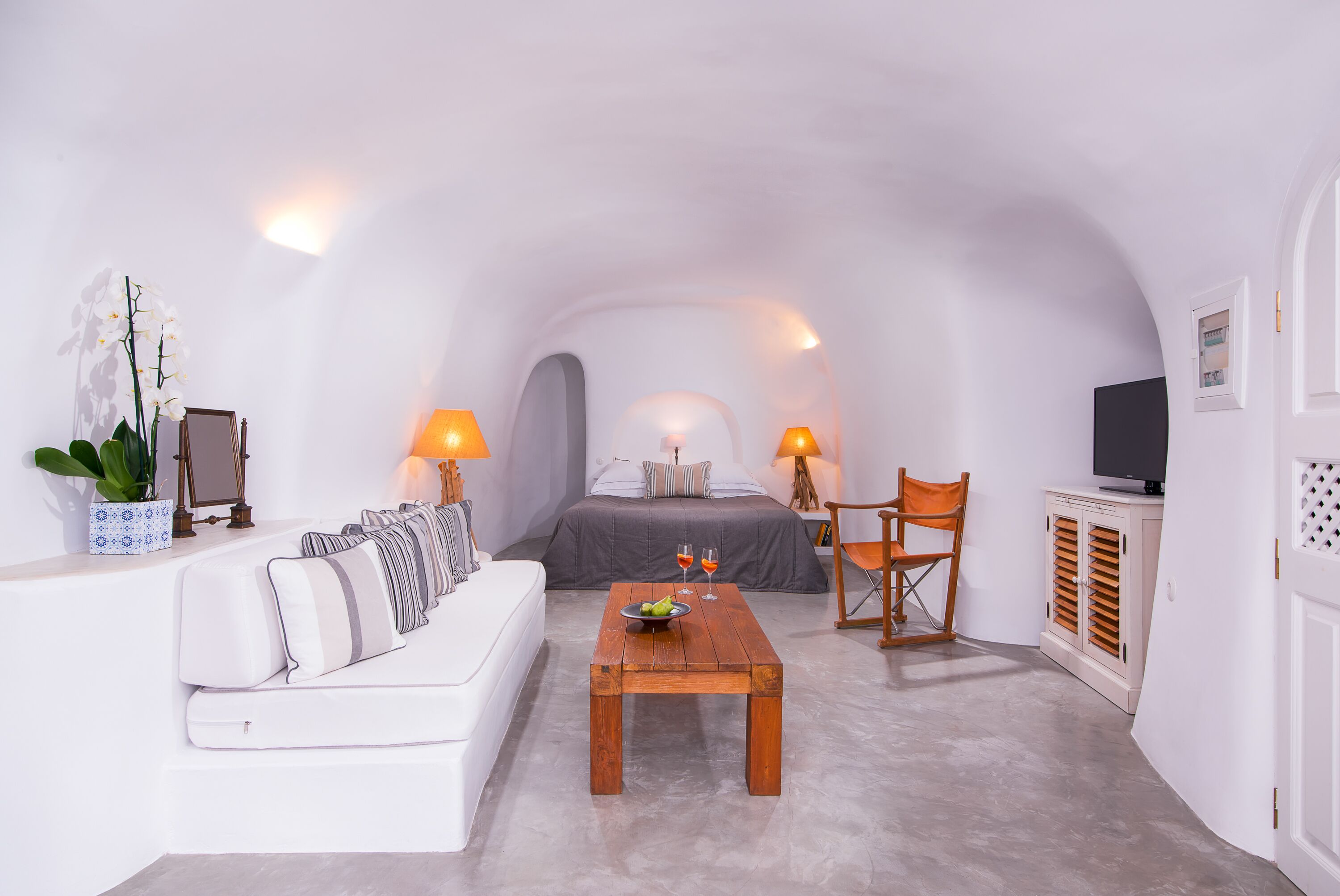A compact, white-walled room with a bed, a sofa, a coffee table, and a TV.