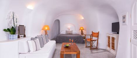 A compact, white-walled room with a bed, a sofa, a coffee table, and a TV.