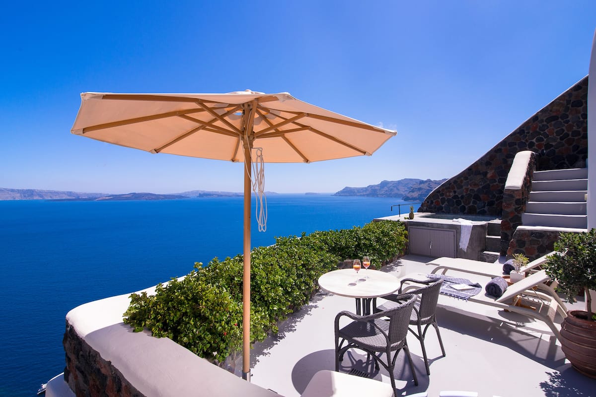A terrace with a table, chairs, and an umbrella overlooking the sea.