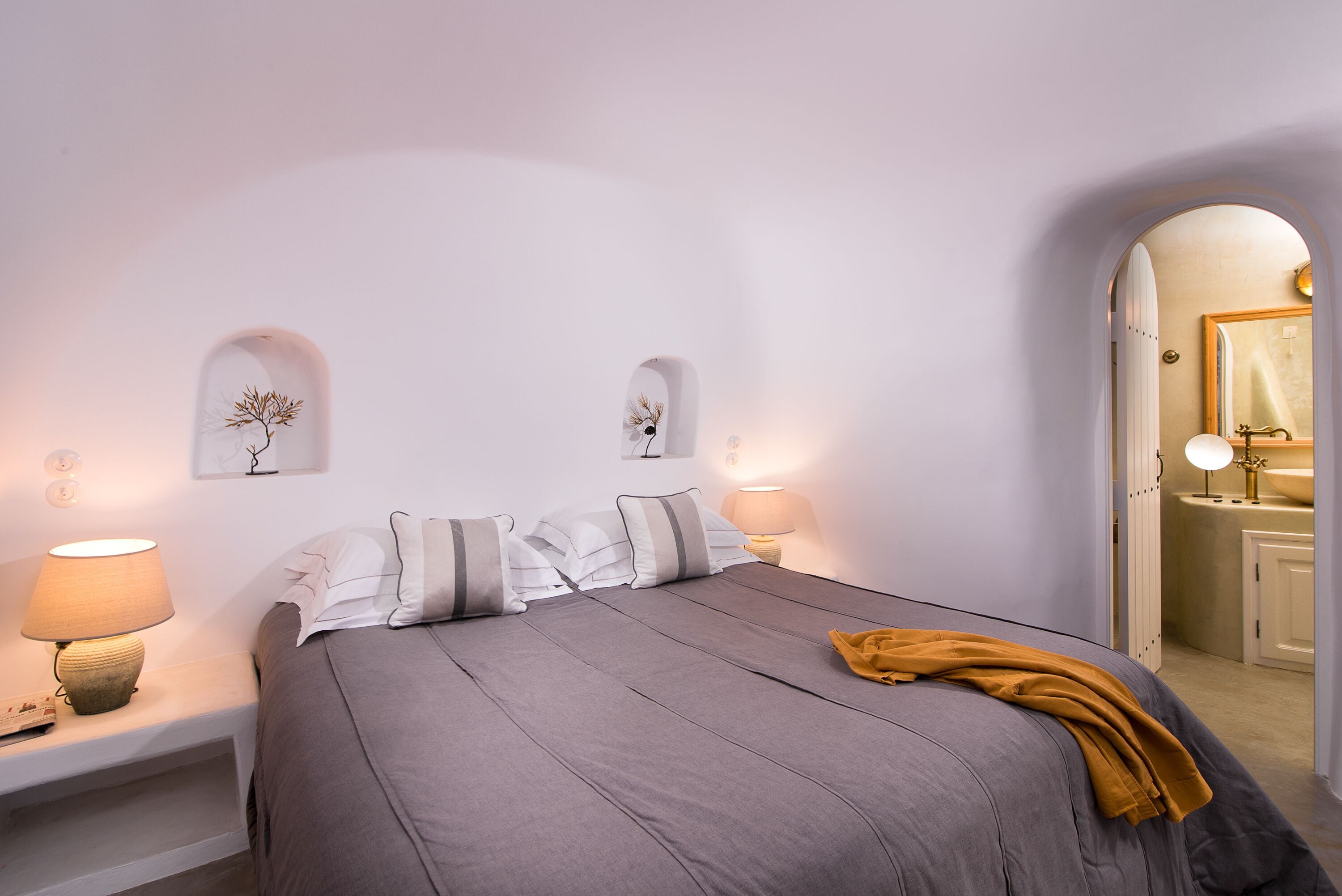 Una camera da letto con un letto, lampade sui comodini, uno specchio e una porta che dà su un bagno.