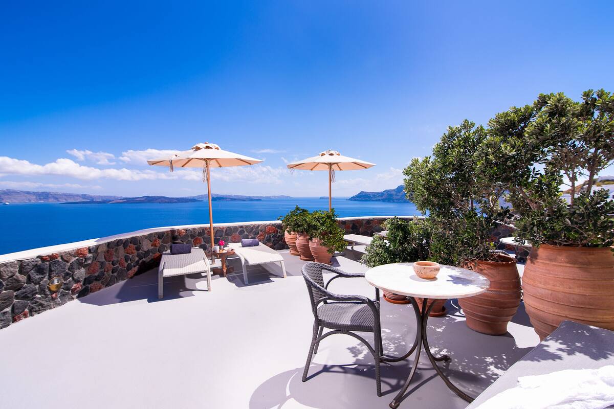 A terrace with a view of the sea, featuring outdoor seating, potted plants, and umbrellas.