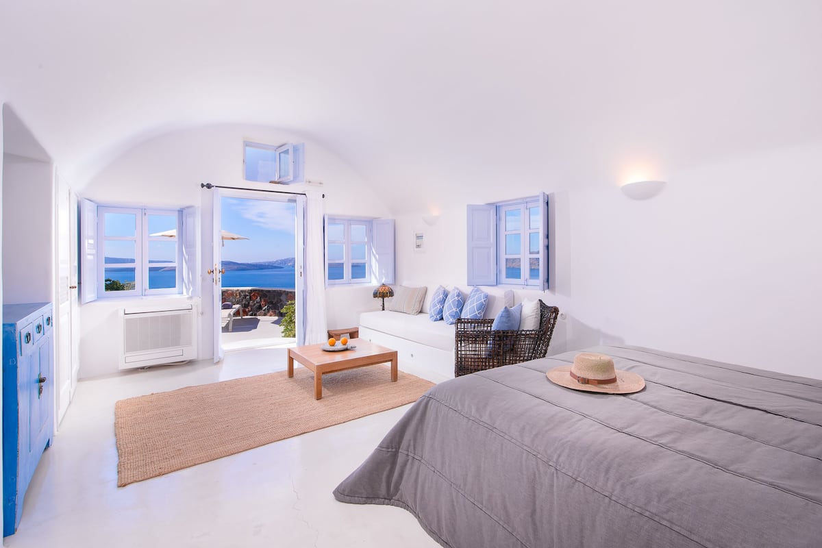 A bright, white room with a bed, a sofa, and a view of the sea.
