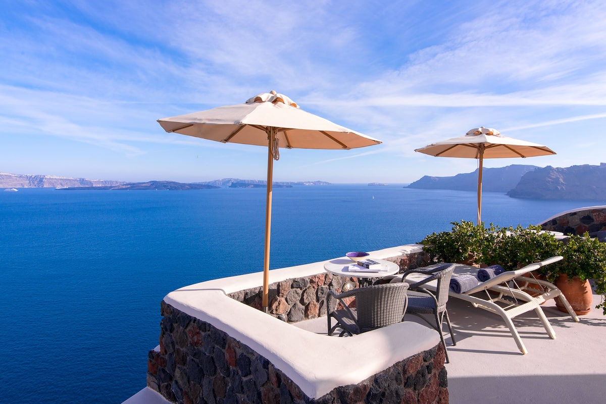 A seaside terrace with two umbrellas, a table, and lounge chairs overlooking the ocean.