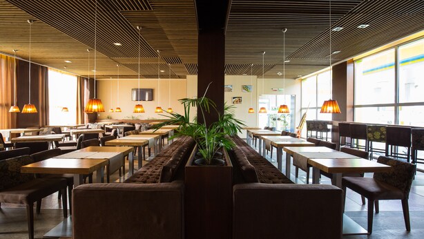 Un restaurante espacioso con techos altos, paneles de madera y ventanas amplias. Mesas y sillas dispuestas para comer.