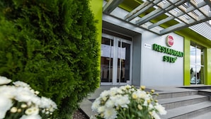 Un edificio moderno con fachada verde y blanca, un letrero que dice 'Restaurant Stop' y escalones que conducen a la entrada.