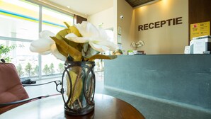 Una mesa de recepción con un florero, un letrero que dice "RECEPTION" y vistas al exterior a través de amplias ventanas.