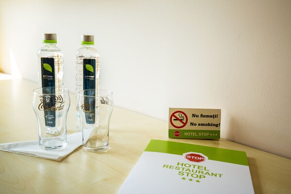 A hotel room with two bottles of water, two glasses, and a 'No smoking' sign on a table.