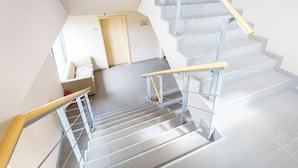 Una escalera con barandales de metal y un pasamanos de madera, que lleva a un cuarto con una puerta y una pequeña mesa.