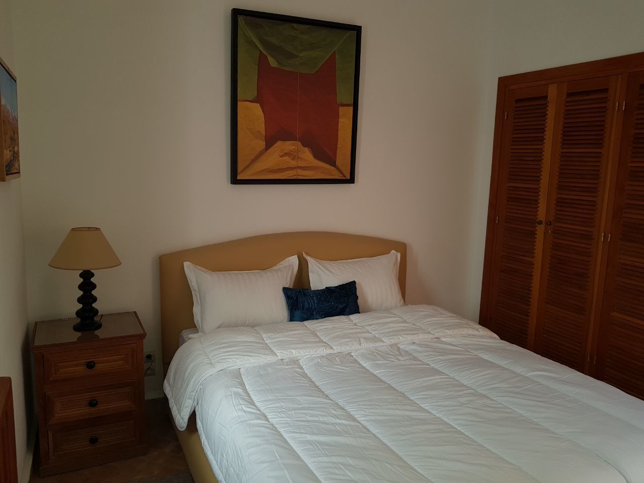 A bedroom with a bed, a nightstand with a lamp, a painting on the wall, and wooden wardrobes.