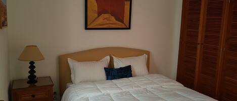 Un dormitorio con cama, una mesita de noche con lámpara, un cuadro en la pared y armarios de madera.