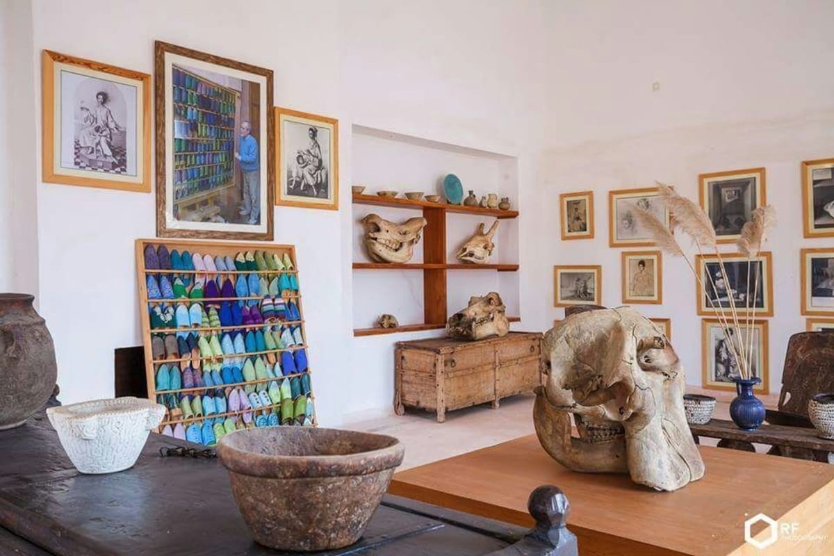 A room with a shoe rack, wooden shelves with pottery, and framed pictures on the walls.