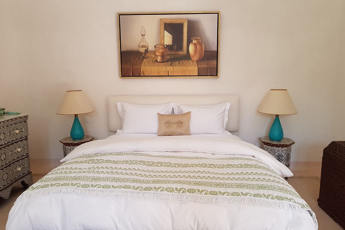 A neatly made bed with a patterned bedspread, two bedside tables with lamps, a small decorative mirror, and a framed artwork above the bed.