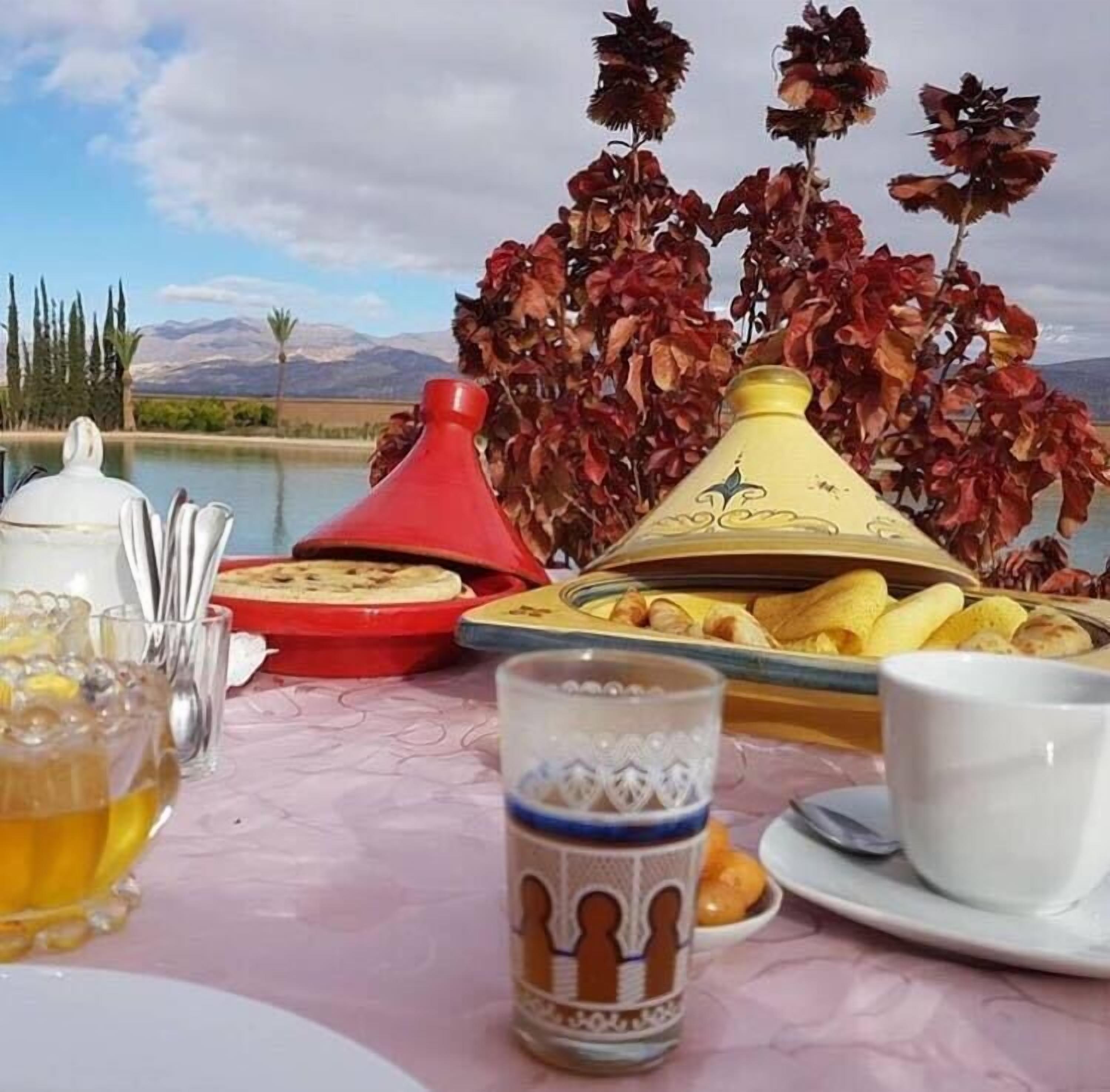 A table set with Moroccan dishes, a teapot, and a view of a lake and mountains.