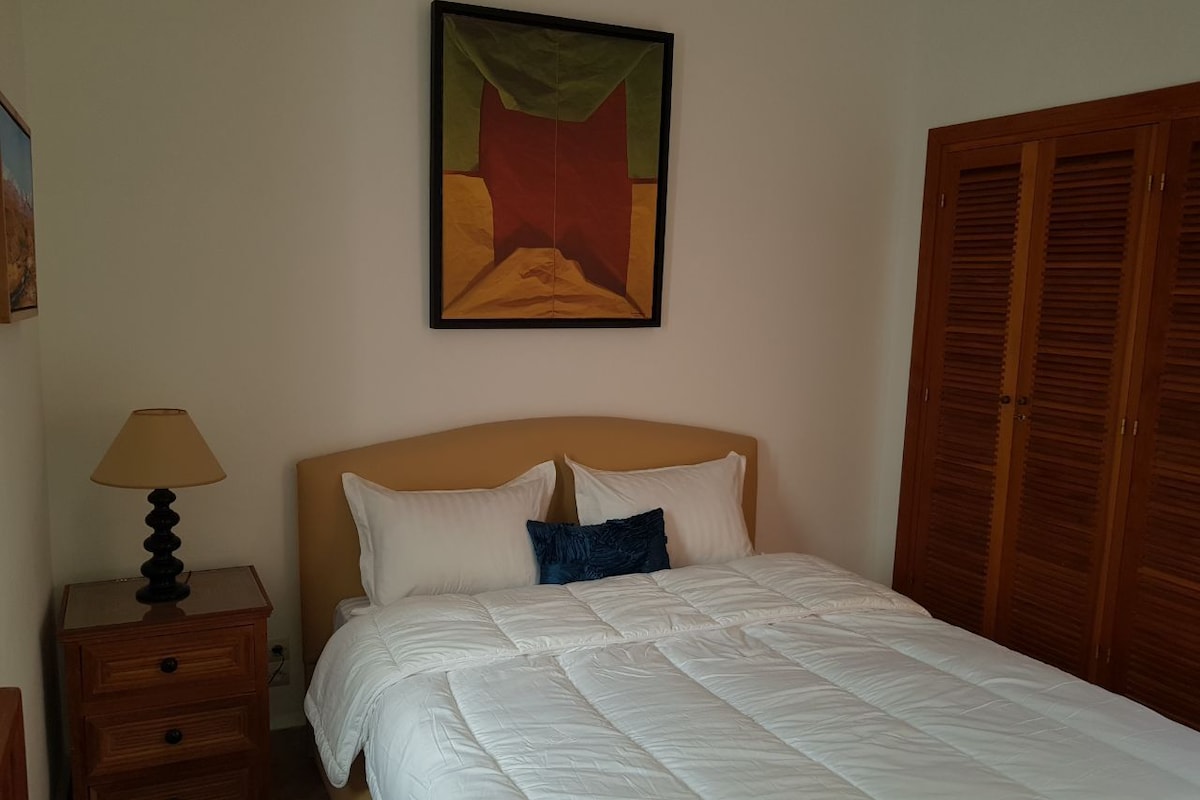 A bedroom with a bed, a nightstand with a lamp, a painting on the wall, and wooden wardrobes.