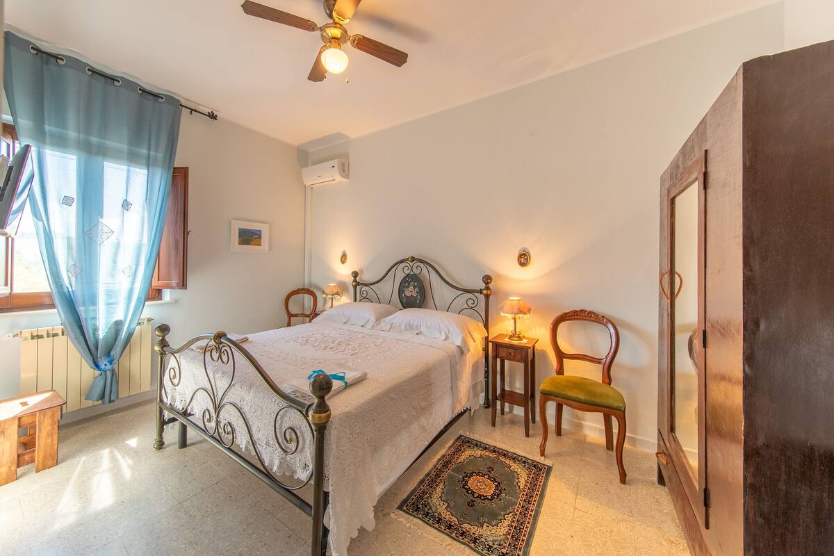 A bedroom with a bed, a chair, a desk, a ceiling fan, and a door.