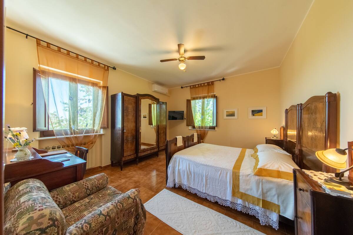 A bedroom with a bed, a desk, a chair, a wardrobe, and a ceiling fan.