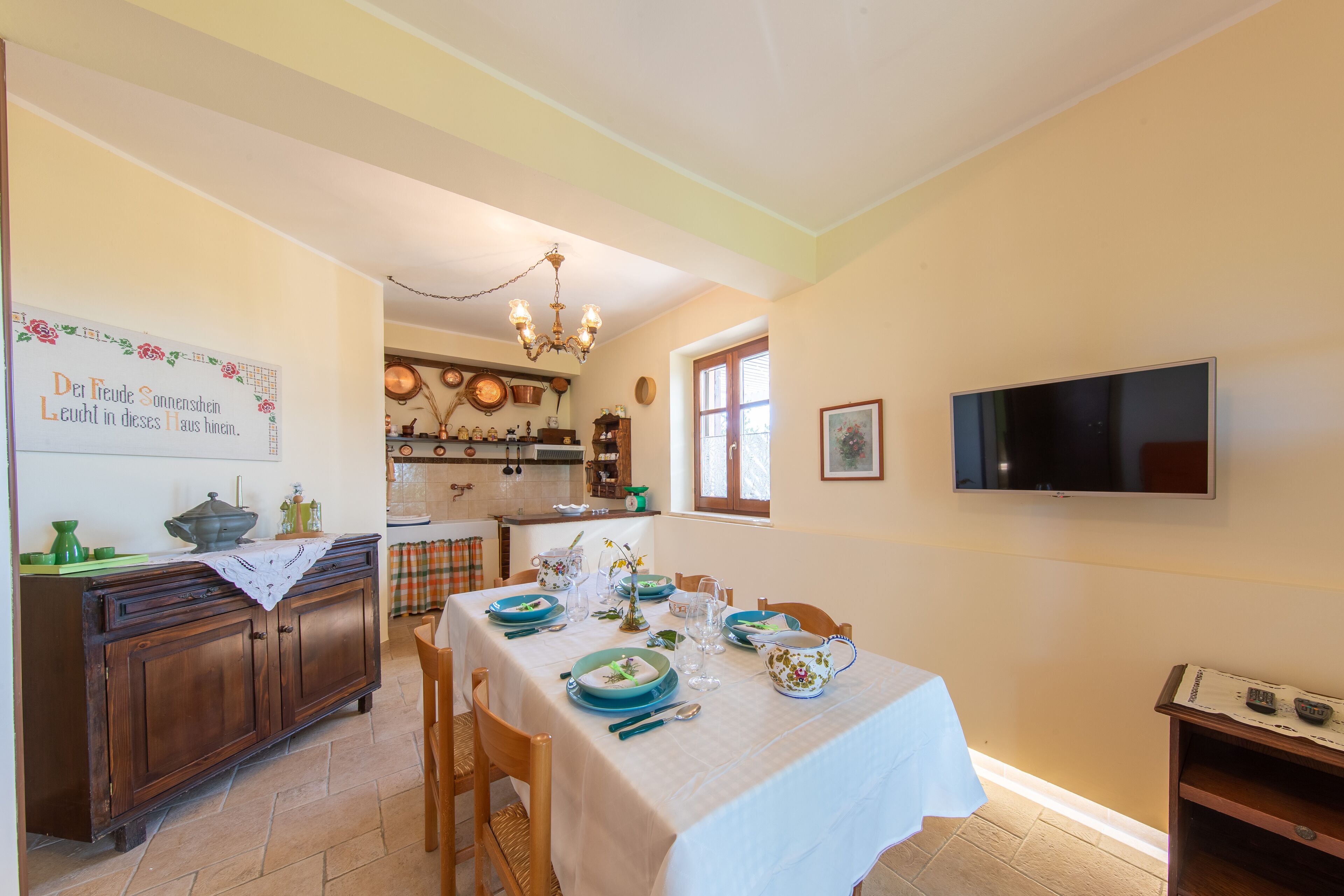 Un coin repas avec une table dressée pour quatre personnes, un buffet en bois et un téléviseur fixé au mur.
