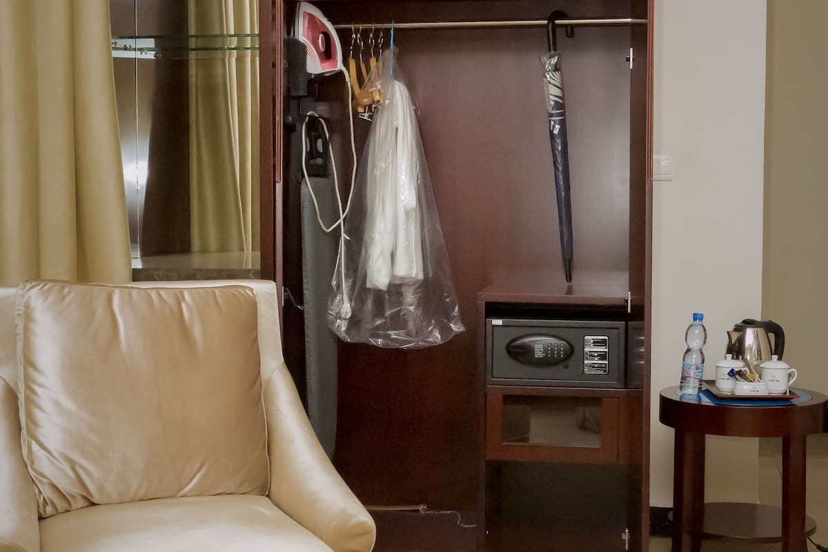 A hotel room with a bed, a leather sofa, a wardrobe, a small table with a kettle, and a mirror.