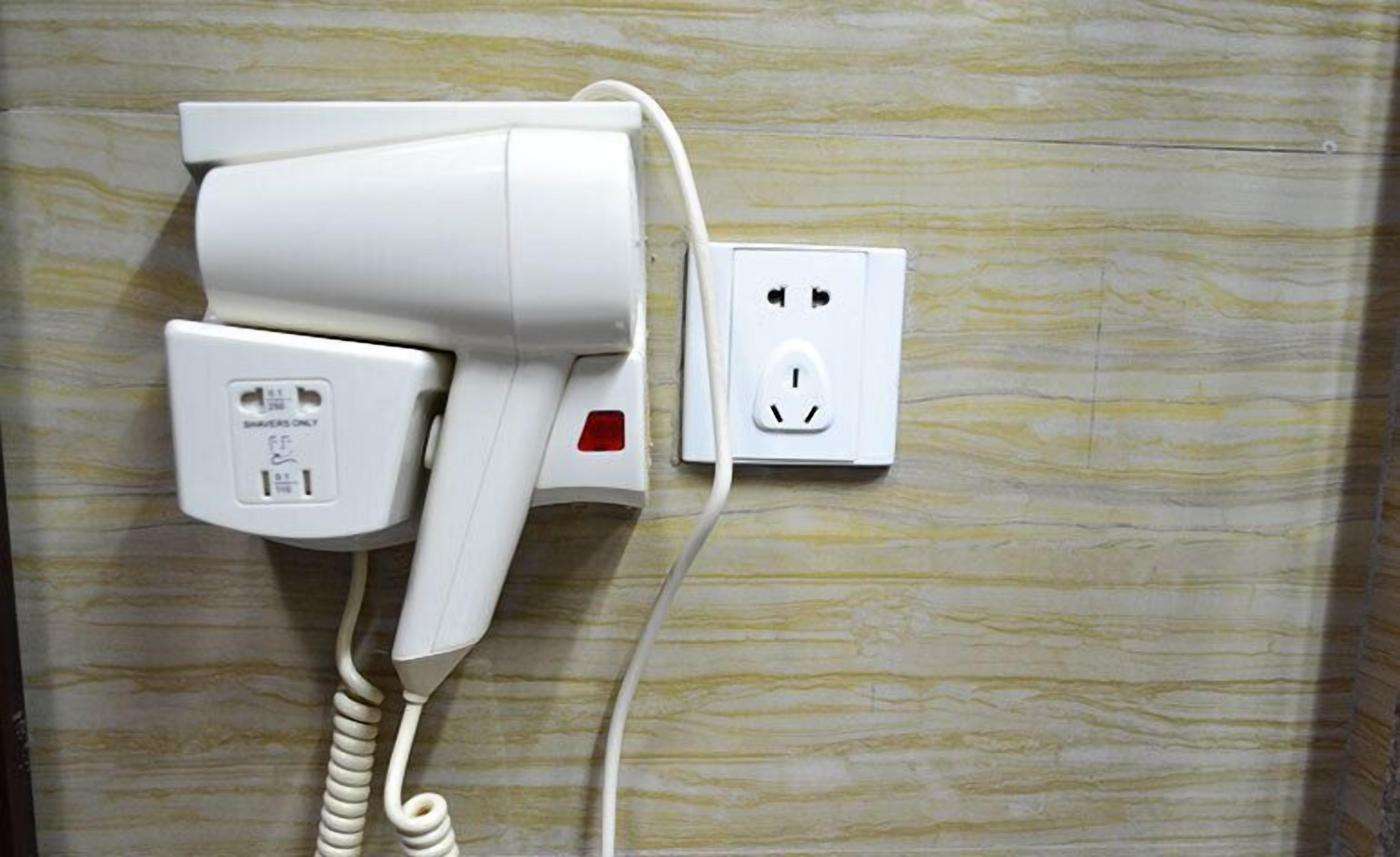 A hairdryer plugged into a wall socket with a power cord.