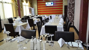 A restaurant with multiple tables set for dining, featuring white tablecloths and black chairs. - Hotel Gloria Inn (Lubumbashi)
