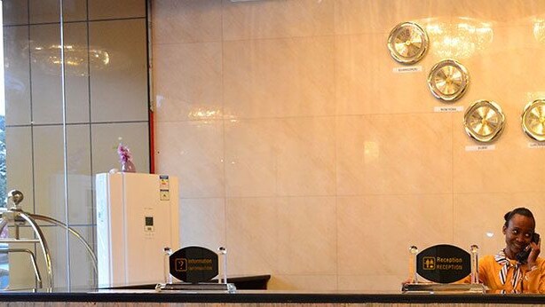 A reception desk with a receptionist, a wall with circular light fixtures, and a sign that reads "Reception." - Hotel Gloria Inn (Lubumbashi)