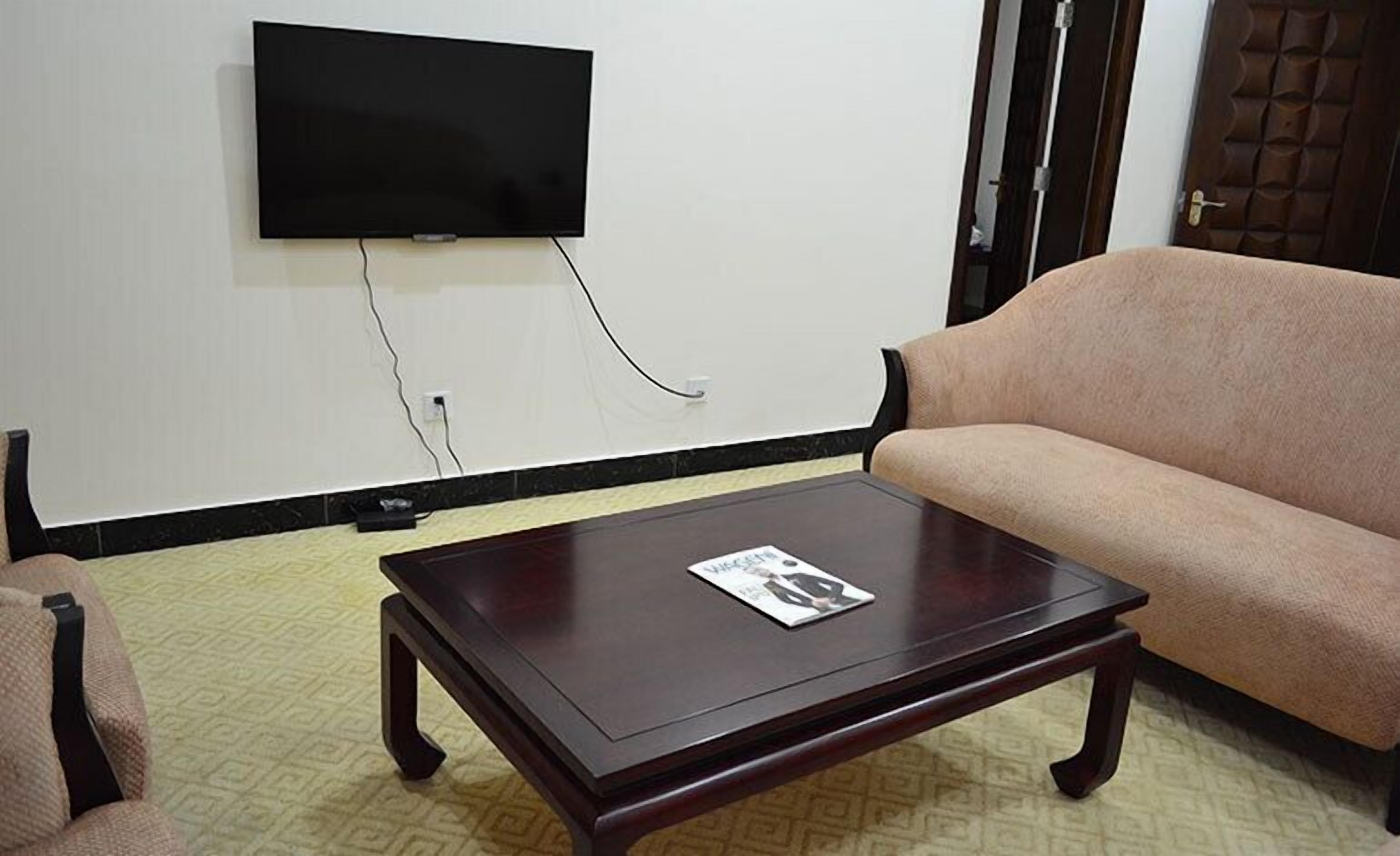 A living room with a dark wooden coffee table, a beige sofa, and a flat-screen TV mounted on the wall.