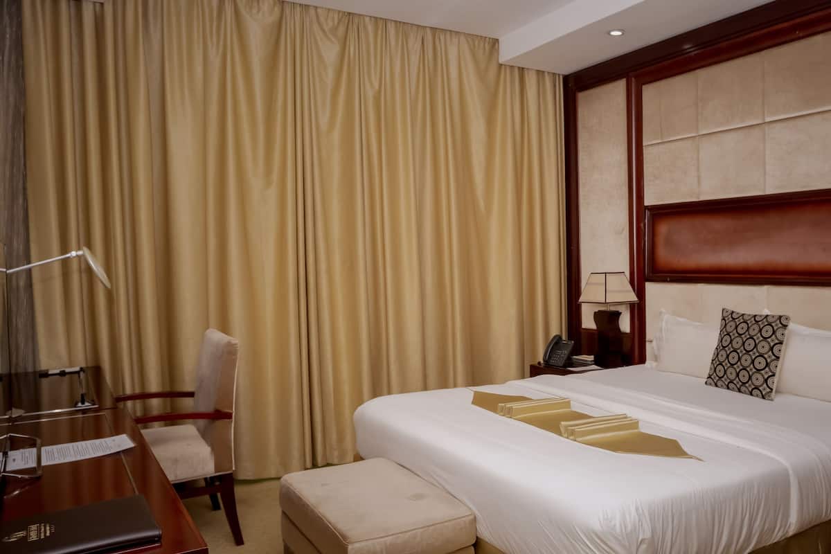 A hotel room with a large bed, a desk, a chair, a telephone, and a lamp.