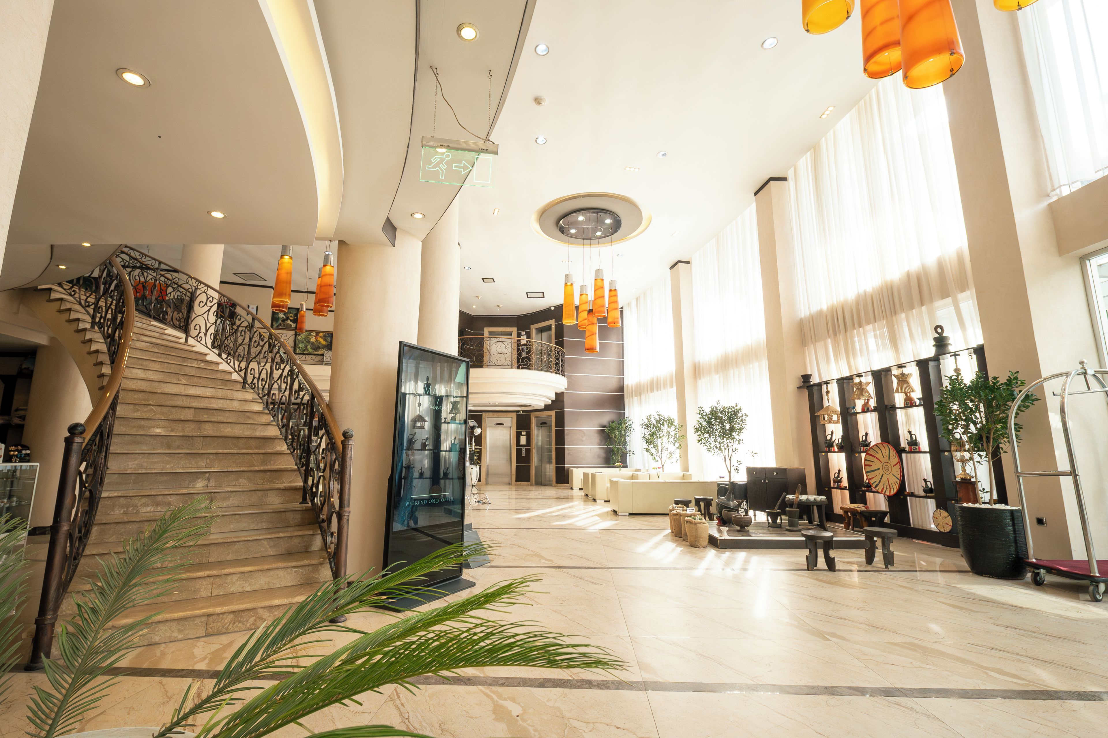 A spacious lobby with a marble floor, a staircase with ornate railings, and a large window allowing natural light.